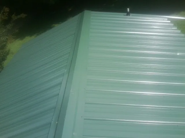 New green metal panels meeting at the ridge of a roof — Flat Roof Repair work by our crew in Atkinson
