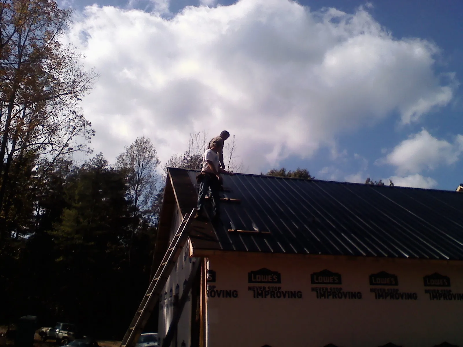Roofer fastening dark metal panels high against a cloudy sky, from a Roof Inspection job in Atkinson
