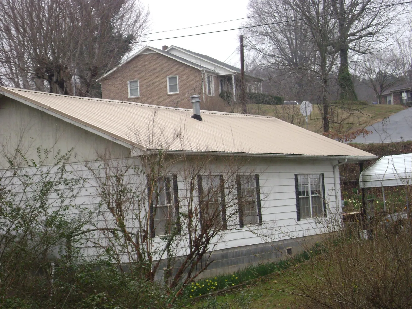 Tan metal roof on a white sided house set into a hillside — Commercial Roofing by Roofing Brothers in Atkinson