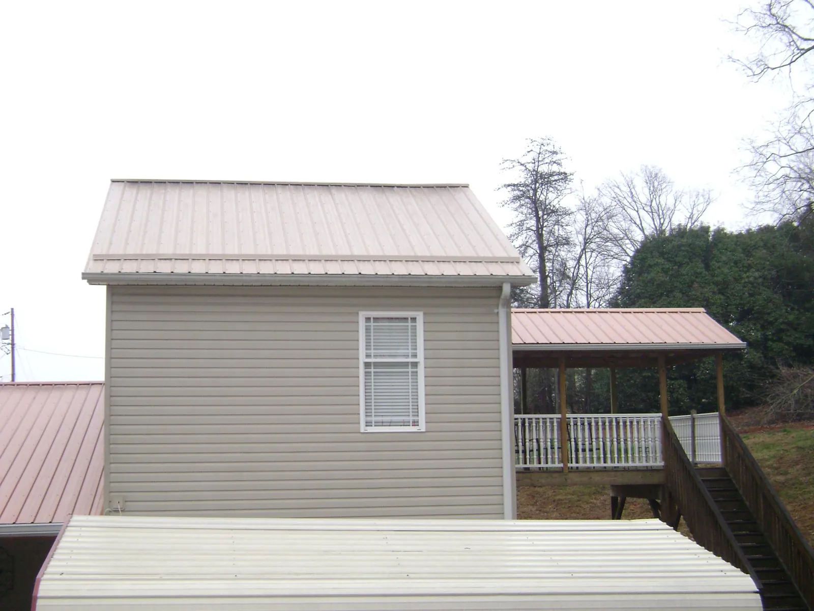 Tan metal roofs on a two story addition and attached porch, from a Roof Replacement job in Atkinson